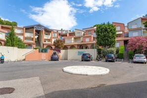 A residential building with multiple balconies, a central courtyard, and parked cars.