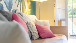 A bed with multiple pillows, a lamp, and a window with a view of greenery. - Apartment 'T2 Meublé Aux Aloès' with Mountain View, Shared Pool and Private Terrace (Cerbère)