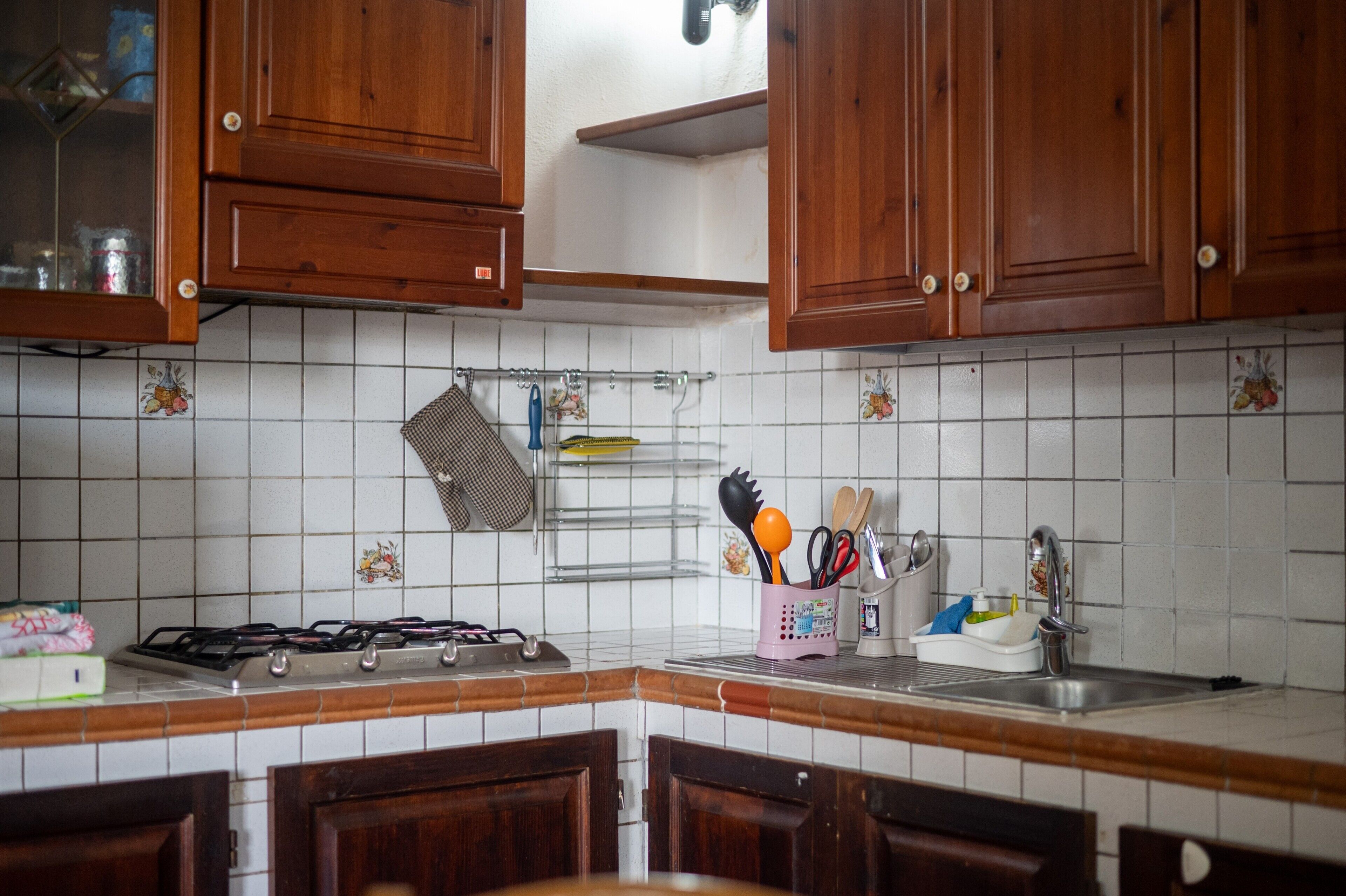 Een keuken met houten kasten, een gasfornuis, een spoelbak en een rek met keukengerei.