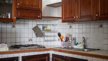 Een keuken met houten kasten, een gasfornuis, een spoelbak en een rek met keukengerei.