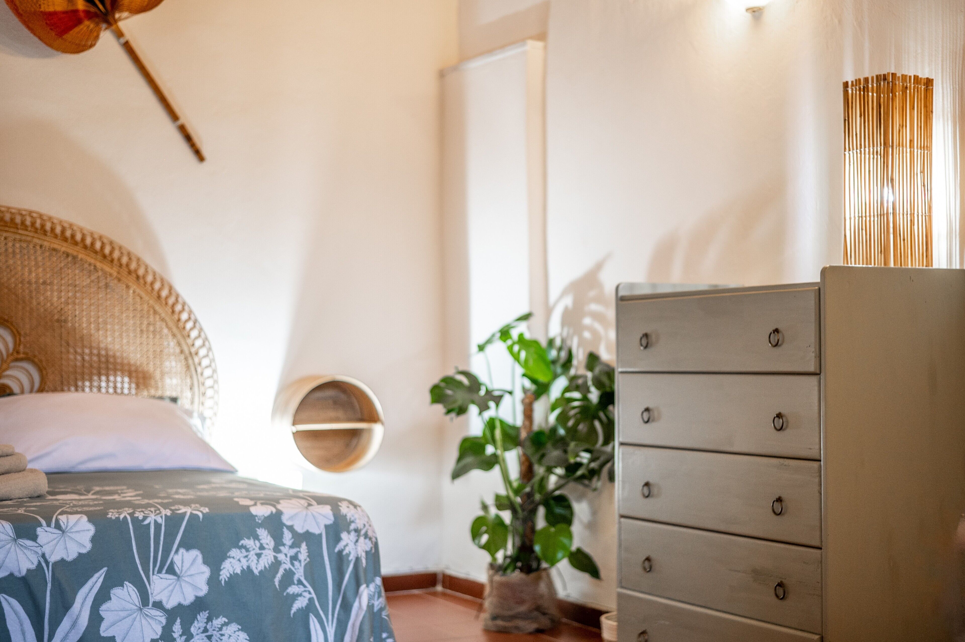 A bedroom with a bed, a dresser, a plant, and a wall-mounted shelf.