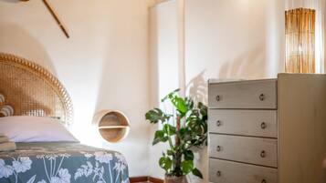 A bedroom with a bed, a dresser, a plant, and a wall-mounted shelf.
