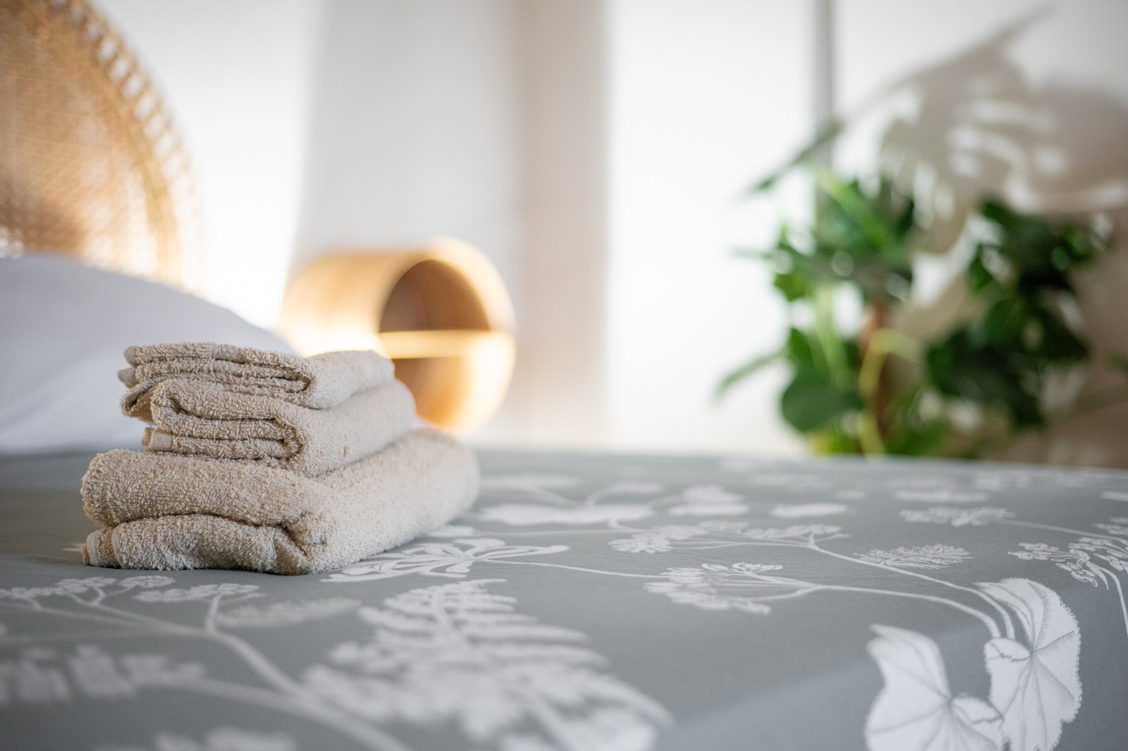 Une pile de serviettes soigneusement pliées est posée sur un lit recouvert d’une couvre-lit à motifs floraux.