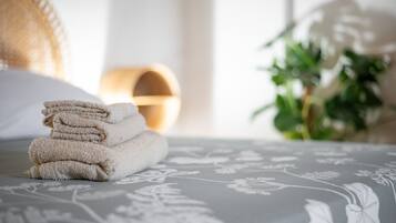 Une pile de serviettes soigneusement pliées est posée sur un lit recouvert d’une couvre-lit à motifs floraux.