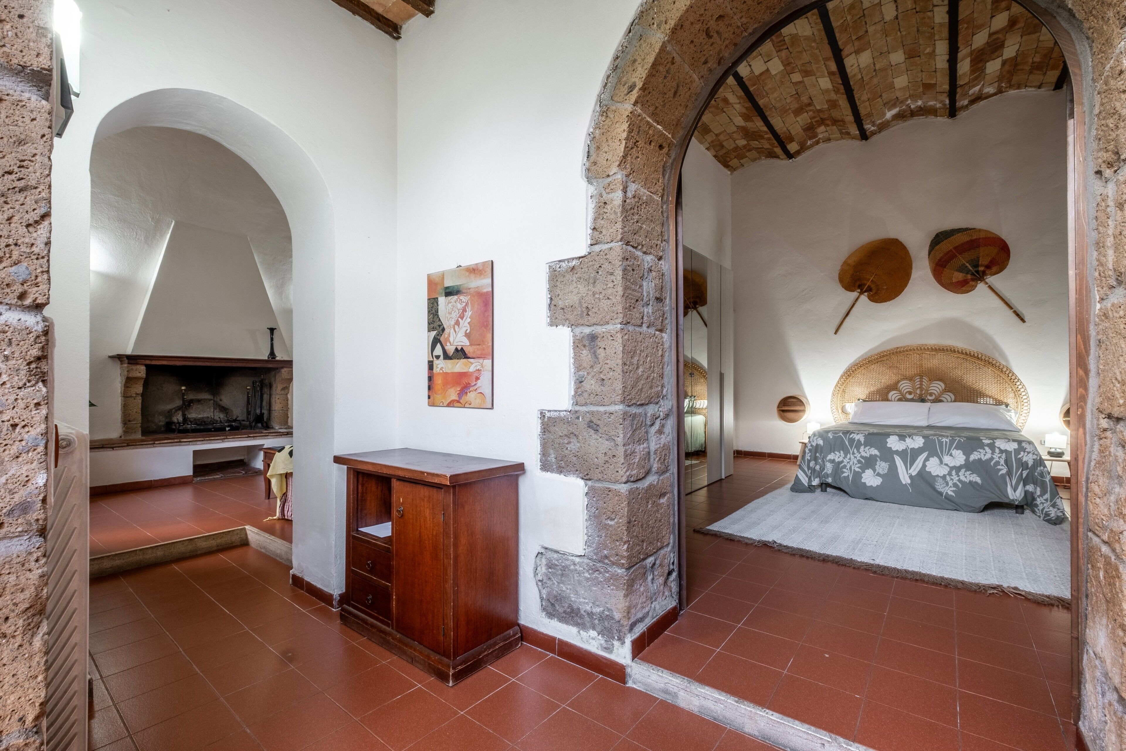 Una habitación con chimenea, una cama con edredón floral, una pared de piedra y un ventilador de techo.