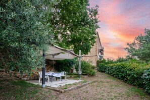 Une terrasse avec une table et des chaises, un luminaire suspendu et un mur en pierre.