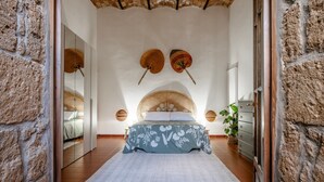 A bedroom with a bed, a woven headboard, a large mirror, and a stone wall.