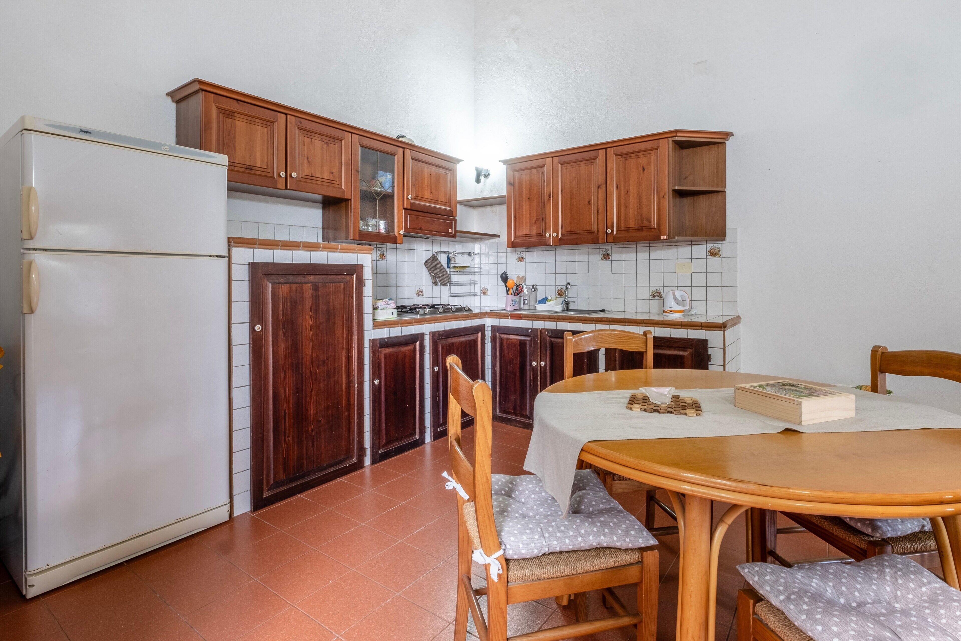 A kitchen with wooden cabinets, a white refrigerator, a dining table with chairs, and a tiled backsplash.