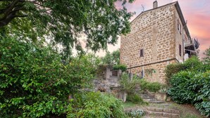 A stone building with a balcony, surrounded by greenery and a stone staircase.