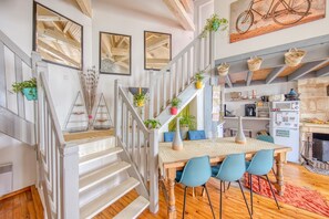Un escalier avec des rampes blanches, une table à manger en bois avec des chaises bleues, et un coin cuisine équipé d’un four à micro-ondes et d’un réfrigérateur.
