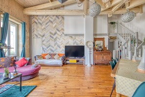 Un salón amplio con una pared de patrón espiga, un sofá, un televisor, una mesa de comedor y una escalera.