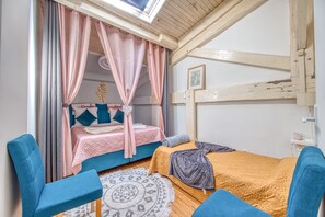 Un dormitorio con una litera, una cama con dosel, un sillón azul, una alfombra estampada y un techo de madera.
