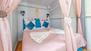 Un dormitorio con una cama, cortinas rosas, un ventilador de pared y un letrero decorativo.