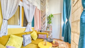 A cozy room with a mustard yellow sofa, a small round wooden table, and a fan. - Dari Apartment – Elegant Getaway in the Heart of Bordeaux (Bordeaux)