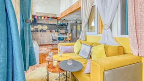 A cozy living room with a yellow sofa, a dining table, and a kitchen area in the background. - Dari Apartment – Elegant Getaway in the Heart of Bordeaux (Bordeaux)