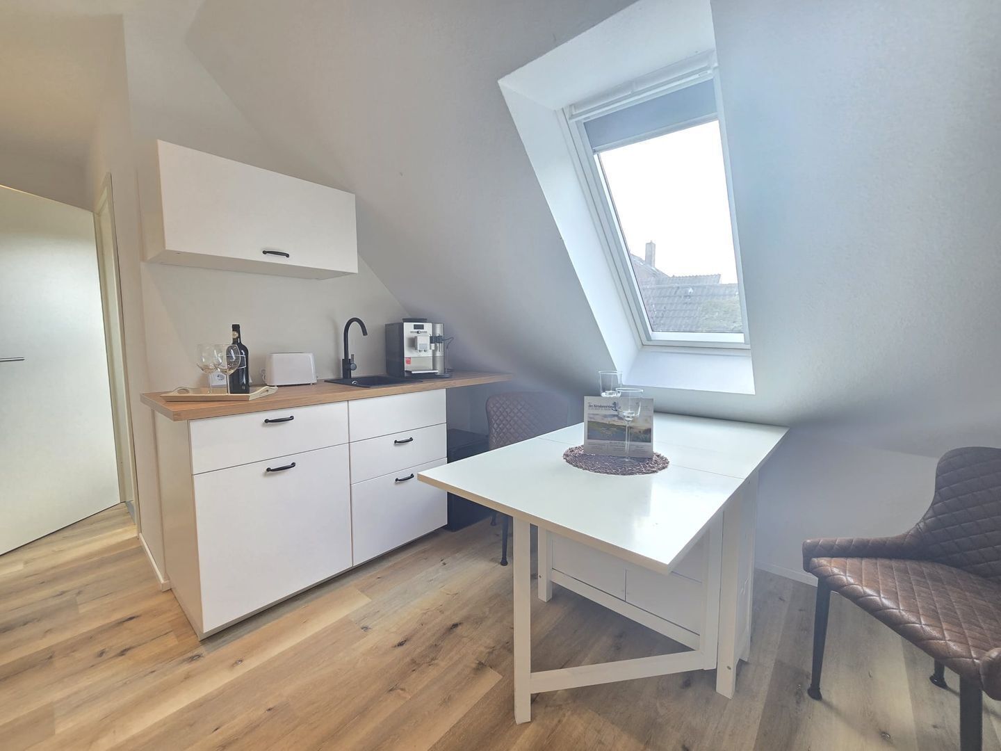 Una cucina moderna con un piano di lavoro bianco, una macchina per il caffè e una bottiglia di vino.