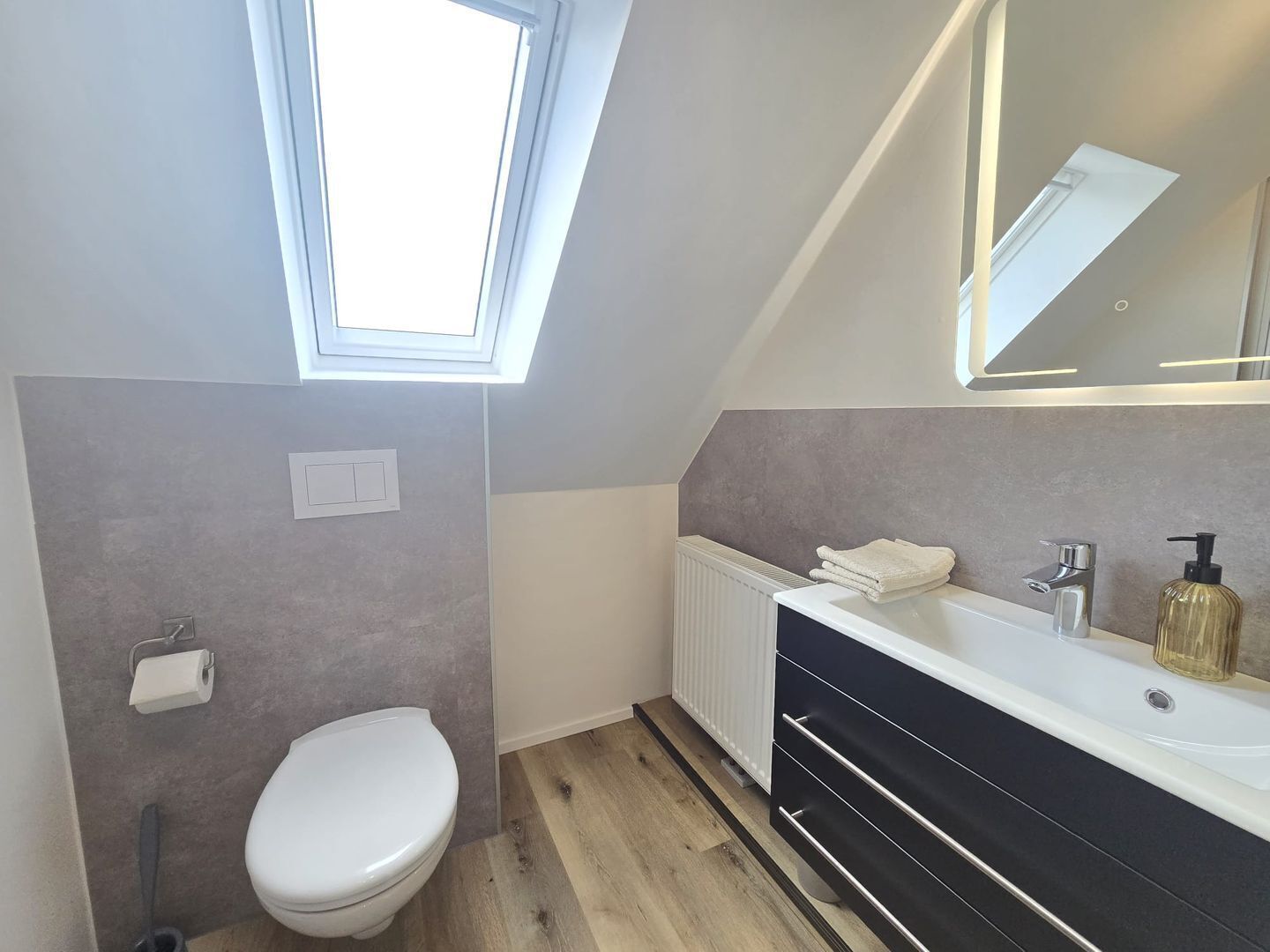 Ein modernes Badezimmer mit Oberlicht, Toilette, Waschtisch mit Spiegel und Handtuchheizkörper.