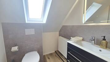 Ein modernes Badezimmer mit Oberlicht, Toilette, Waschtisch mit Spiegel und Handtuchheizkörper.