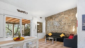 A room with a stone wall, a wooden ceiling, a white table with chairs, a black sofa with yellow cushions, and a hanging light fixture.
