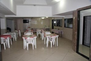 Un espace repas avec plusieurs tables et chaises, une cuisine à l’arrière-plan et une porte-fenêtre coulissante.