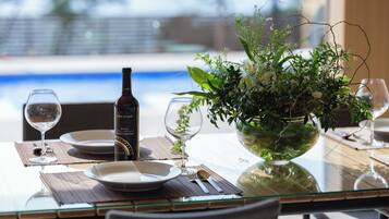 A dining table with a bottle of wine, a glass, a bowl of greenery, and a view of a pool.