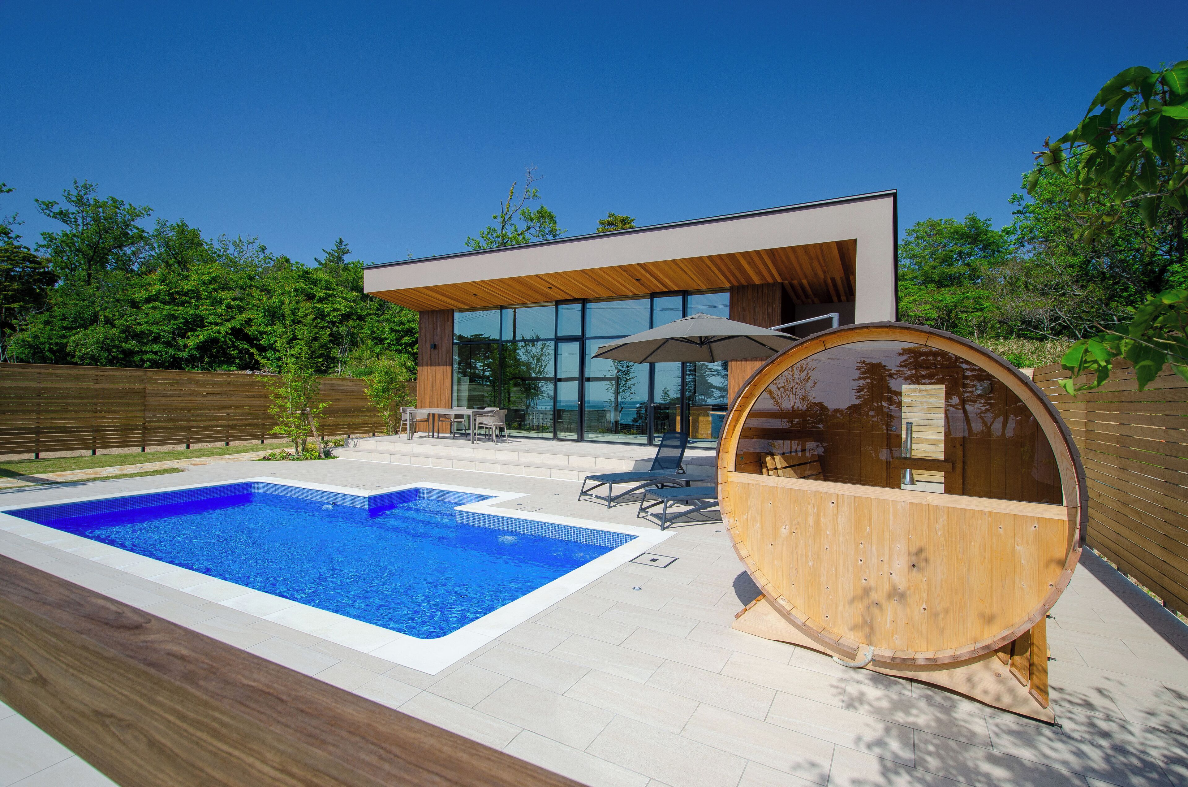 A modern house with a swimming pool, outdoor seating, and a wooden barrel structure.
