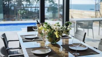 A dining table set for two with a vase of flowers, a glass of water, and a view of the ocean.