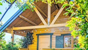 A wooden cabin with a pitched roof, a window with shutters, and a porch area with string lights.