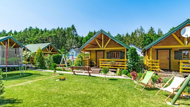 A row of wooden cabins with green roofs, surrounded by a well-maintained lawn and small trees.