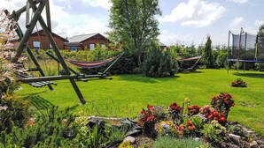 A well-maintained garden with a hammock, a swing set, and a trampoline.