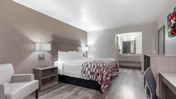 Ein modernes Hotelzimmer mit einem großen Bett, einem Schreibtisch, einem Sessel und einem Spiegel.