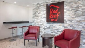 Ein Empfangsbereich eines Red Roof Inn mit einer Steinsäule, zwei roten Ledersesseln und einer Theke.