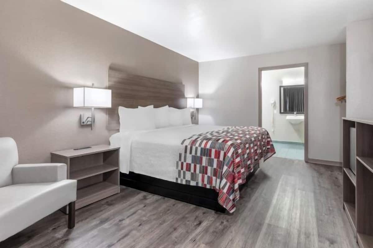 Una habitación de hotel moderna con cama, mesitas de noche, una silla y un armario.