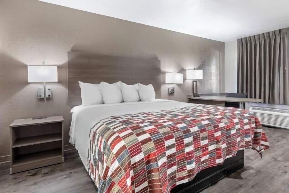 Habitación de hotel moderna con cama, mesitas de noche, lámparas y un amplio ventanal con cortinas.