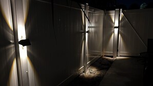 Un espacio al aire libre cercado, con paneles iluminados en las paredes, un camino de hormigón y una estructura metálica al fondo.