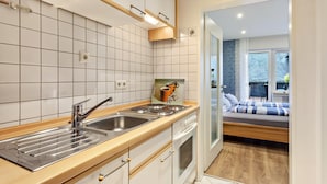 A modern kitchen with a sink, stove, and oven, a dining area with a table and chairs, and a bedroom with a bed and window. - Haus Schönblick - Apartment 5 with Mountain View, Private Terrace and Wi-Fi (Willingen (Upland))