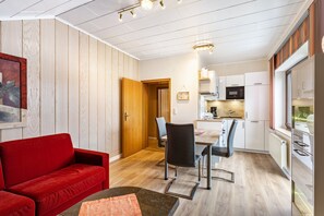 A modern kitchen with white cabinets, a dining area with a red sofa, and a wooden door leading to another room. - Haus Schönblick – “Appartment 6” with Mountain View, Balcony and Wi-Fi (Willingen (Upland))