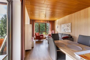 A modern interior with a wooden ceiling, a dining area with a table and chairs, a sofa, and a view through large windows. - Haus Schönblick - "Apartment 9" with Mountain View, Balcony and Wi-Fi (Willingen (Upland))