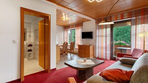 A modern living room with a red carpet, a stone coffee table, a sofa, a TV, and a dining area with chairs and a table. - Haus Schönblick - Apartment 10 with Mountain View, Balcony and Wi-Fi (Willingen (Upland))