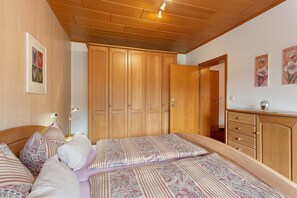 Un dormitorio con un armario de madera, una cama con ropa de cama estampada y una mesita de noche con una lámpara.