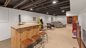 A modern kitchen with a wooden bar and stools, a foosball table, and a cozy seating area with a sofa and a coffee table. - URBAN RETREAT - 4 BEDROOM HOUSE, FAMILY FRIENDLY with ARCADE, GAMES.. (West Des Moines)