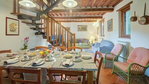 A dining area with a wooden staircase, a table set for a meal, wicker chairs, and a view of the living room. - Home Romeo Private Pool Surrounded by Nature, Borgo a Mozzano, Italy (Borgo a Mozzano)