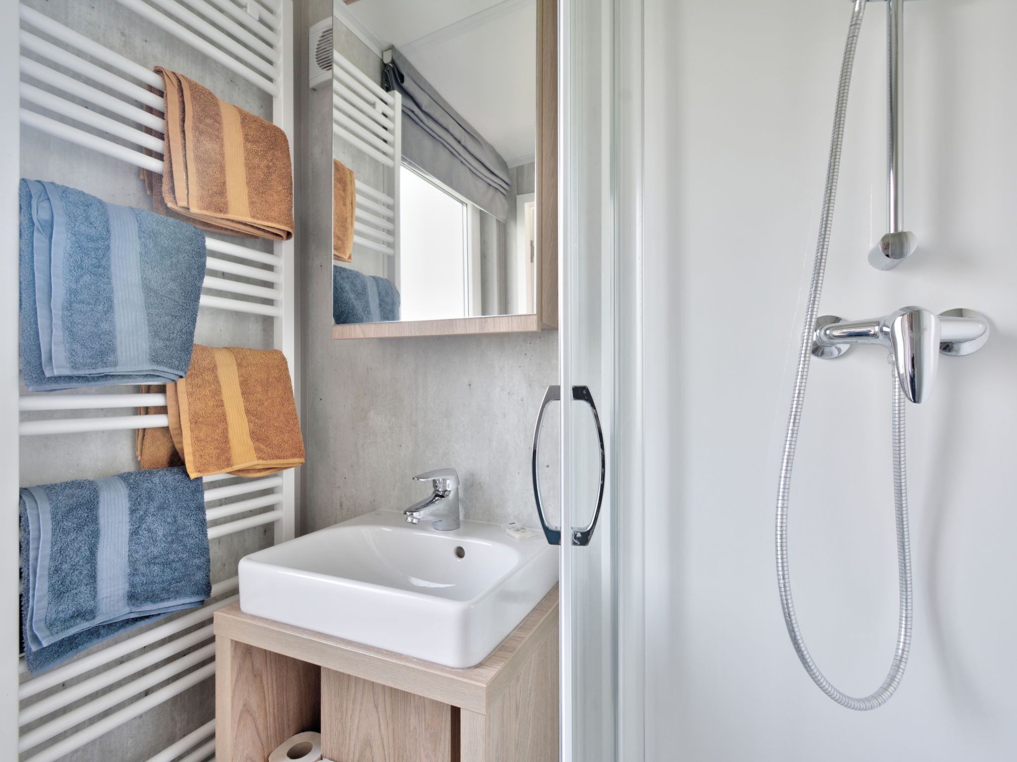 Un baño moderno con un lavabo blanco, un cabezal de ducha manual y toallas en un perchero.