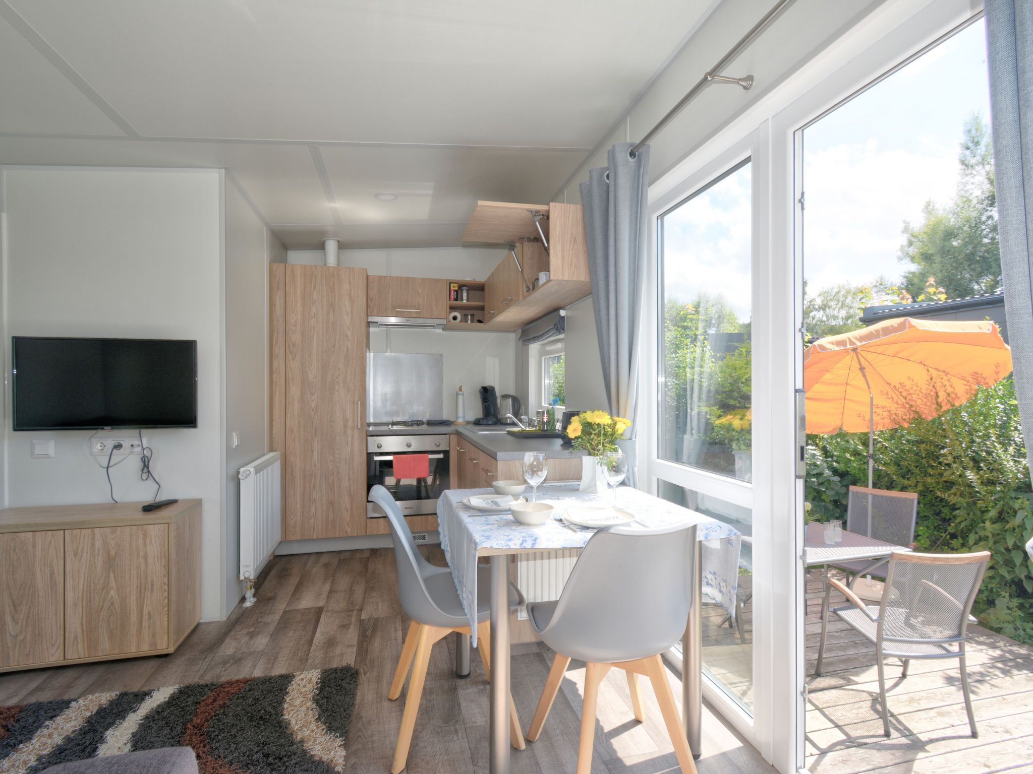 A modern kitchen with wooden cabinets, a built-in oven, and a flat-screen TV.