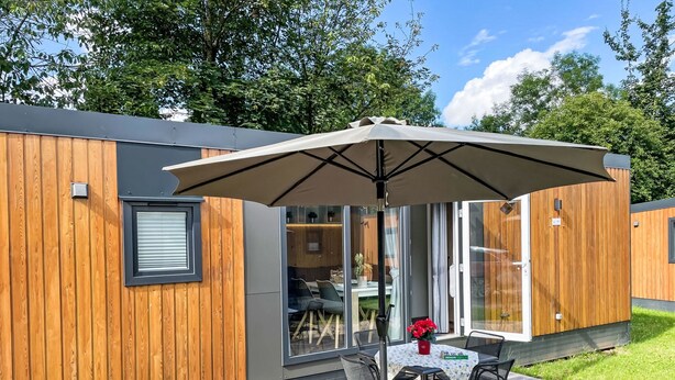 Ein modernes Holzgebäude mit einer Terrasse, einem Tisch mit Stühlen und einem großen Sonnenschirm.