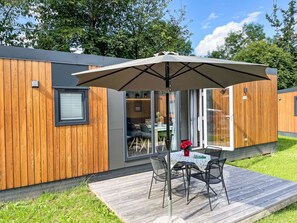 Un bâtiment moderne en bois doté d’une terrasse, d’une table avec des chaises et d’un grand parasol.