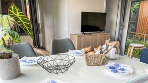 Ein moderner Essbereich mit einem Glastisch, Stühlen, einem Fernseher und Blick auf Grünflächen.