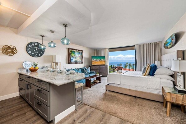 A modern hotel room with a kitchen area, a balcony with a view, and a large bed.