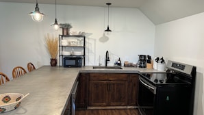 Een moderne keuken met een centraal eiland, houten kastjes, een ingebouwde oven, een koffiezetapparaat en hanglampen.