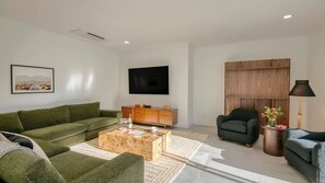 A modern living room with a green sofa, a wooden coffee table, a TV, and a wooden cabinet.